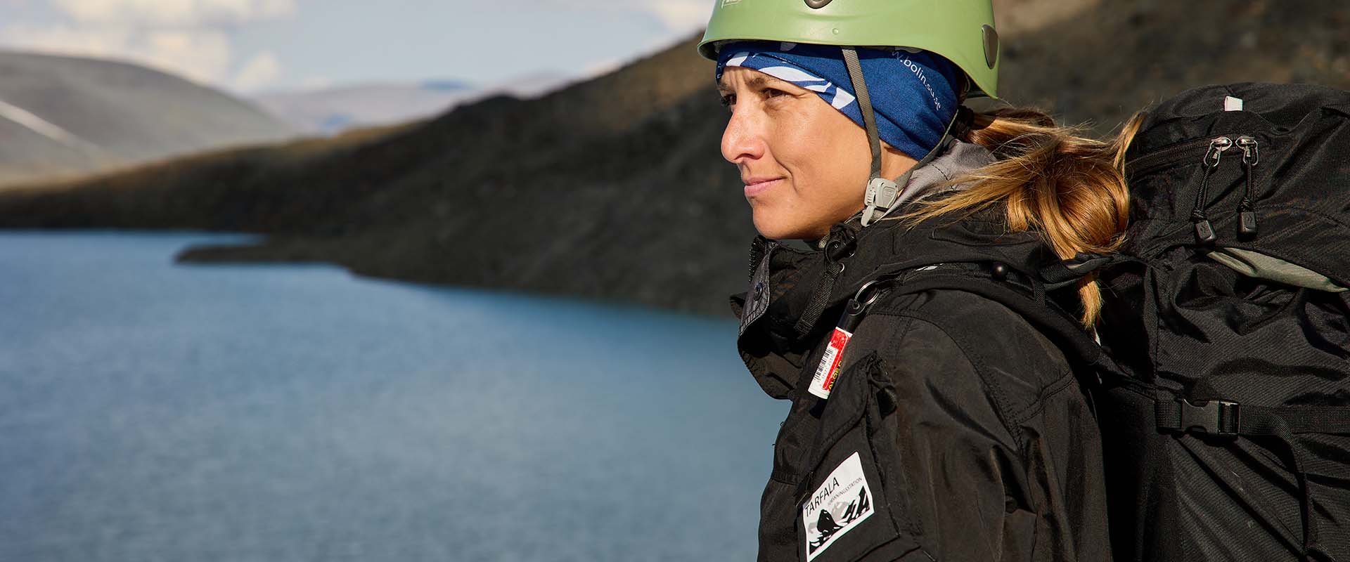 A woman from Tarfala Research Station wearing Taiga workwear near a lake and mountain 